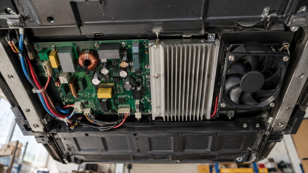 The underside of an induction cooktop showing a power inverter board, its heat sink and the cooling fan mounted beside it