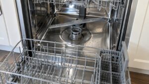 The inside of a dishwasher tub with the lower rack pulled out and the cylindrical filter visible at the bottom